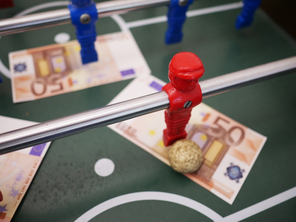 Rotes Männchen eines Tischkickers steht mit Ball auf einem 50-Euro-Schein
